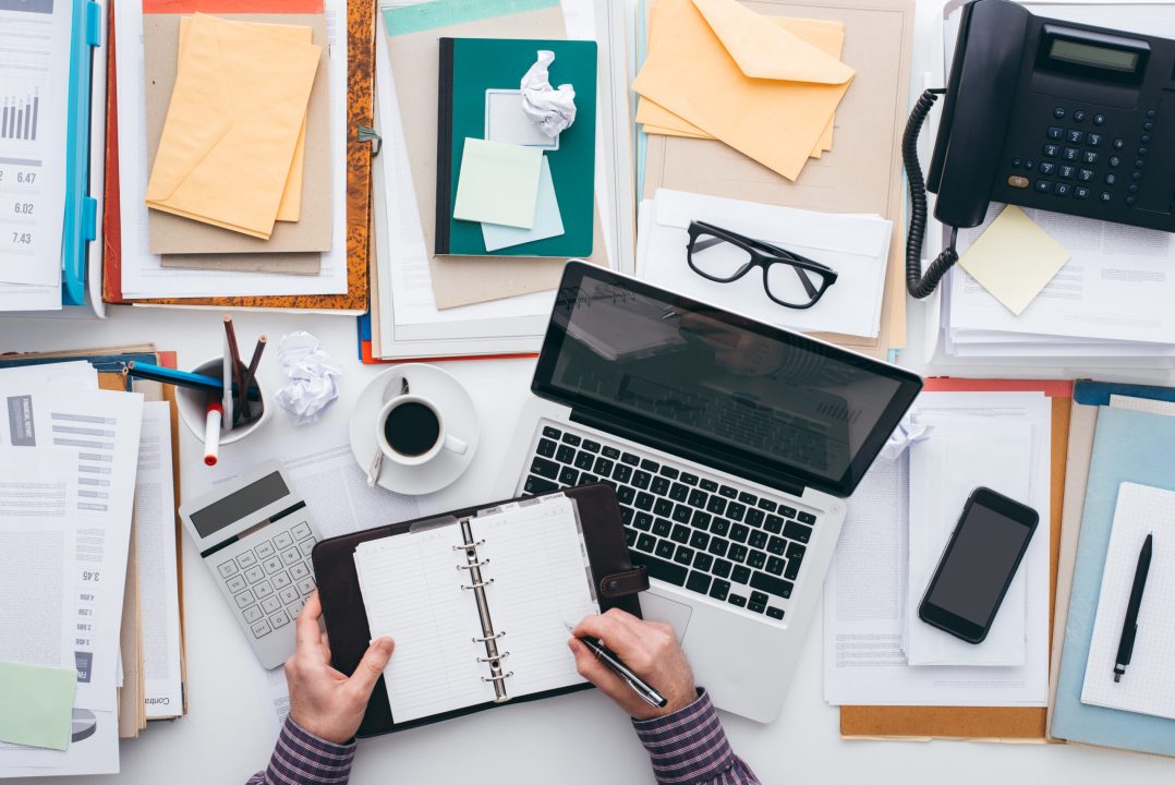 Businessman scheduling appointments on his organizer and full desktop with paperwork and a laptop, flat lay